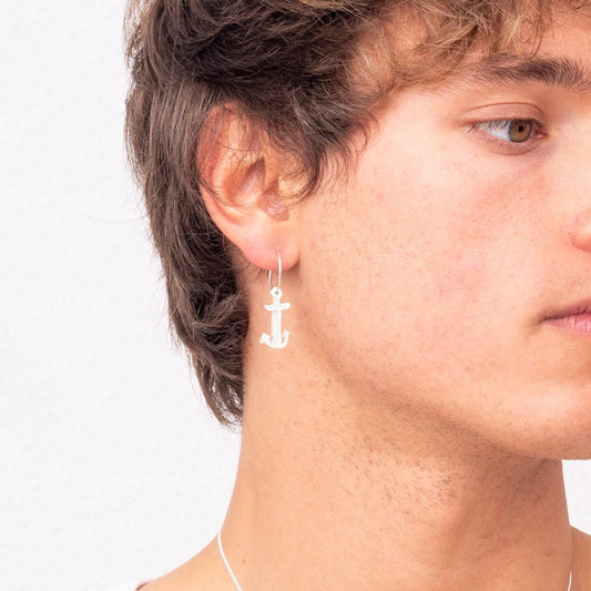 A person with wavy brown hair wearing a white tank top, an Underwater Anchor Handmade Nautical Hoop Earring by Angela Lago, and a necklace.