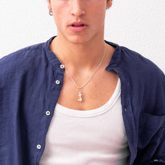A young man with tousled hair wears a blue button-up shirt over a white tank top and the handmade "Underwater Anchor Pendant" by Angela Lago, standing in front of a white background.