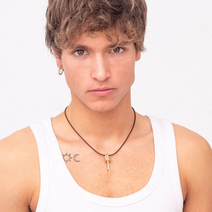 Young man with blonde hair wearing a white tank top, small hoop earrings, and a Nautical golden knot pendant - Ballestrinque S necklace, posing against a plain white backdrop. Has tattoos on both shoulders.