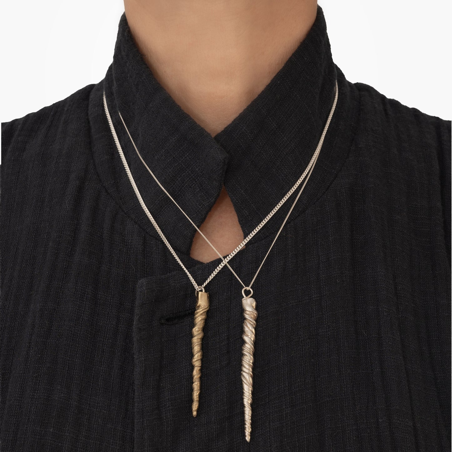 Person wearing a black textured garment with a high collar and two pendant necklaces—one handmade by Angela Lago with a straight rectangular sterling silver pendant and the other featuring the Narwhal Tusk Handmade Tooth Pendant inspired by narwhal tusk jewelry.