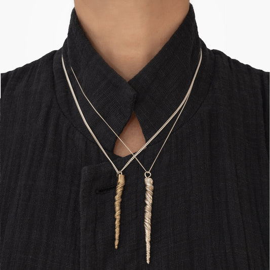 Person wearing a black textured garment with a high collar and two pendant necklaces—one handmade by Angela Lago with a straight rectangular sterling silver pendant and the other featuring the Narwhal Tusk Handmade Tooth Pendant inspired by narwhal tusk jewelry.