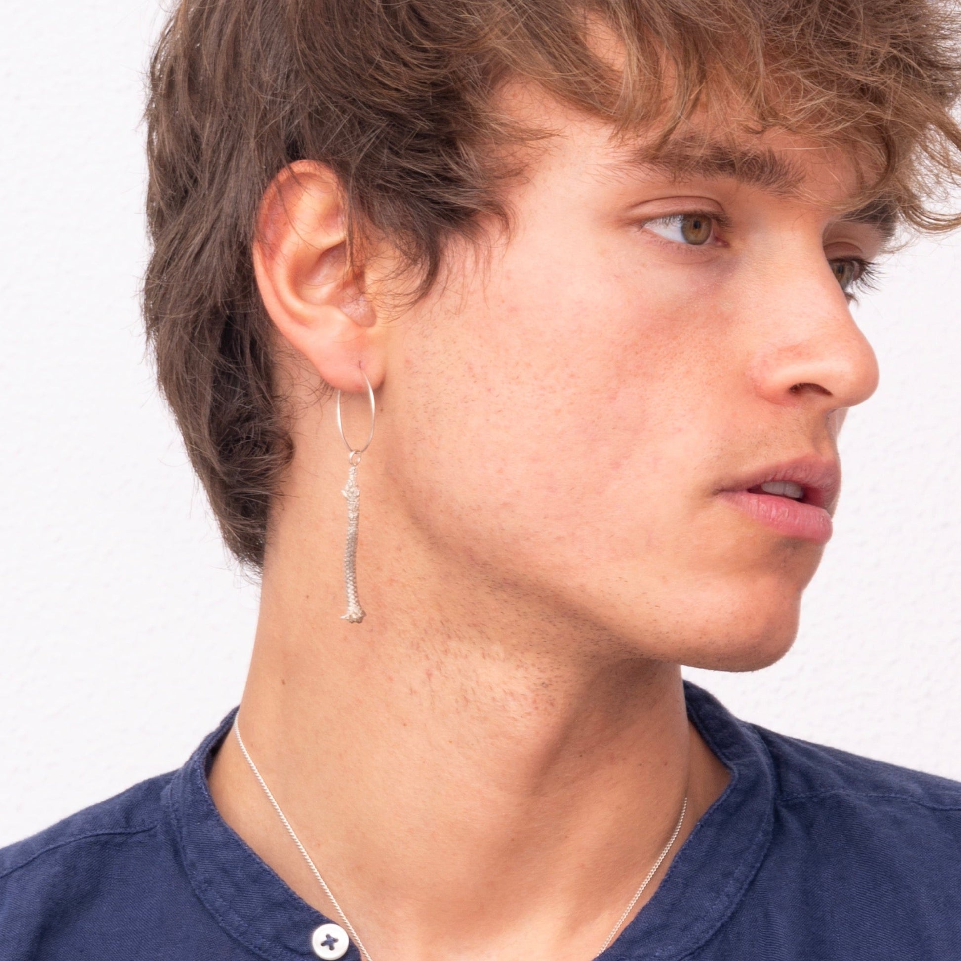 A young person with short brown hair, wearing a blue button-up shirt and a Thin Hoop Nautical Earring with Sterling Silver Rope, looking to the side.