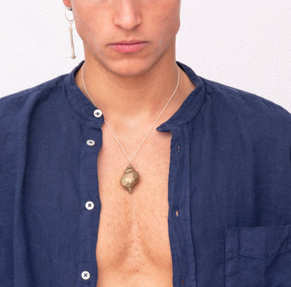 Young man with light brown hair wearing a navy blue shirt, a single earring, and the Nautical Handcrafted Seashell One of A Kind Pendant Nº 1 by Angela Lago poses against a plain white background.