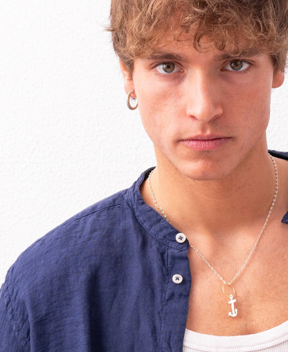 A young person with curly hair wears a blue shirt over a white tank top and a necklace with an anchor pendant, sporting the Nautical hoop Corto Maltese inspired: Creole Rope Earring size S, handmade by Angela Lago, while posing against a white background.